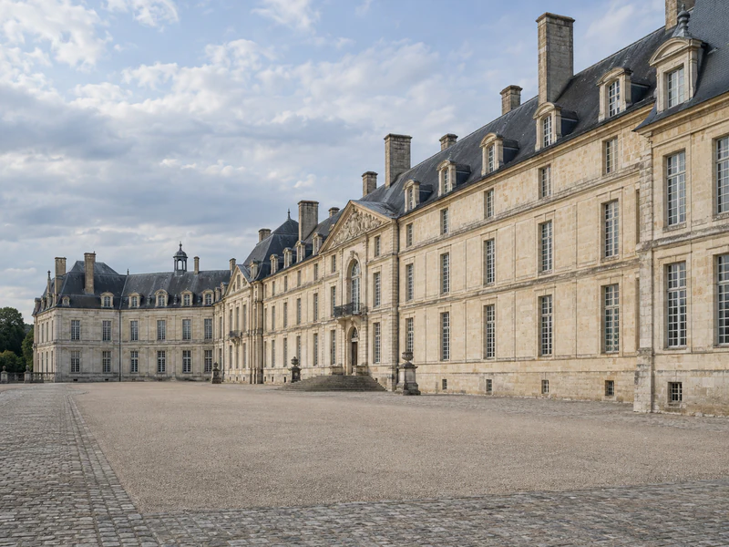 Longue façade de château en pierre de taille, cour et toitures d'ardoise